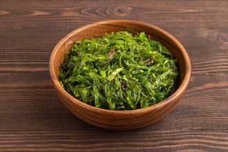 Chuka seaweed salad in wooden bowl on brown wooden background. Side view, close up