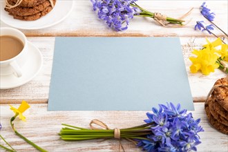 Blue paper sheet with oatmeal cookies, spring snowdrop flowers bluebells, narcissus and cup of