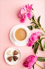 Cup of cioffee with chocolate candies, pink peony flowers on pink pastel background. top view, flat