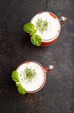Tomato juice with basil and sour cream in glass on a black concrete background. Healthy drink
