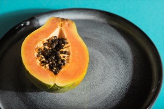 Ripe cut papaya on gray plate on blue pastel background. Side view, close up, hard light. Tropical,