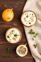 Yoghurt with granadilla and mint in wooden bowl on brown wooden background and linen textile. top