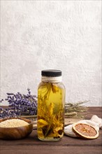 Sunflower oil in a glass jar with various herbs and spices, lavender, sesame, rosemary on a brown