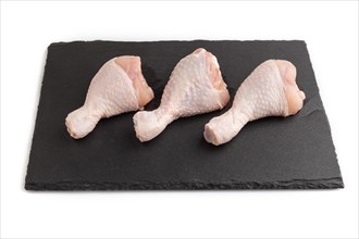 Raw chicken legs on a black slate cutting board isolated on white background. Side view, close up