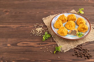 Fried manti dumplings with pepper, basil on brown wooden background and linen textile. Side view,
