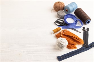 Sewing accessories: scissors, thread, thimbles, braid on white wooden background. Side view, copy