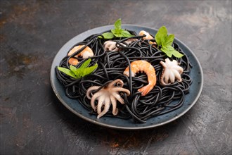 Black cuttlefish ink pasta with shrimps or prawns and small octopuses on black concrete background.