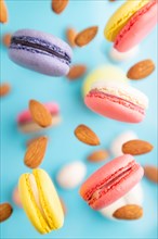 Multicolored flying macaroons and almonds eggs frozen in the air on blurred blue background. top