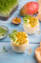 Mango yogurt with passionfruit and cilantro microgreen in glass on blue wooden background with