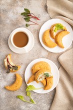 Homemade salted crescent-shaped cheese cookies, cup of coffee on brown concrete background and