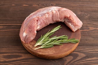 Raw pork with herbs and spices on a wooden cutting board on a brown wooden background. Side view,