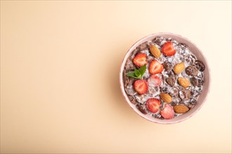 Chocolate cornflakes with milk, strawberry and almonds in ceramic bowl on pastel orange background.