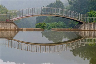 Foot bridge over a small pond with reflection in the water with trees in the background and a dull