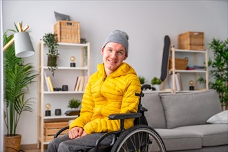 Portrait of cheerful disabled man in wheelchair smiling at camera in the living room at home