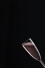 A champagne glass filled with rose sparkling wine against a black background