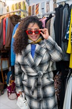 Vertical portrait of a fun woman looking trough sunglasses shopping in a vintage clothes store