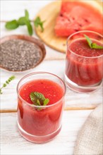 Watermelon juice with chia seeds and mint in glass on a white wooden background with linen textile.