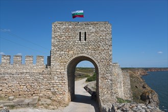 Stone archway of an old fortress with waving flag next to a steep cliff, fortress ruins, Cape