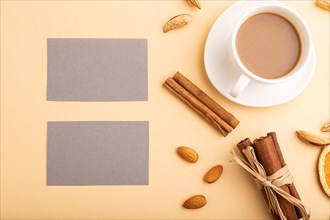Composition of gray paper business cards, almonds, cinnamon and cup of coffee. mockup on orange