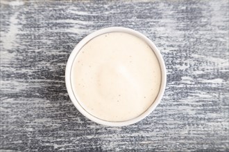 Ceramic sauce bowl with mayonnaise on a gray wooden background. Top view, close up, copy space
