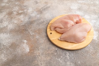 Raw chicken breast on a wooden cutting board on a brown concrete background. Side view, copy space
