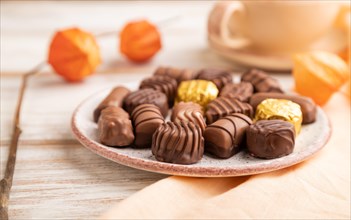 Chocolate candies with cup of coffee and physalis flowers on a white wooden background and orange