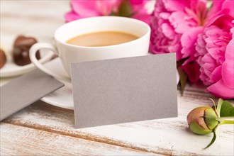 Gray business card with pink peony flowers and cup of coffee on white wooden background. side view,