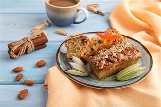 Caramel and almond cake with cup of coffee on blue wooden background and orange linen textile. side