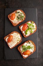 Red beet bread sandwiches with cream cheese, tomatoes and microgreen on black concrete background.