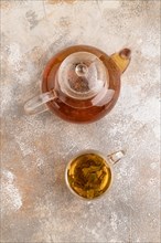 Red tea with herbs in glass teapot on brown concrete background. Healthy drink concept. Top view,