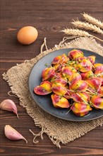 Rainbow colored dumplings with pepper, herbs, microgreen on brown wooden background and linen