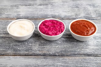 Ceramic sauce bowls with horseradish, tomato sauce and mayonnaise on a gray wooden background. Side