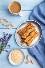 Crumble cookies with seasme and almonds on ceramic plate with cup of coffee and blue linen textile