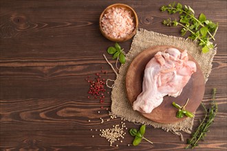 Raw turkey wing with herbs and spices on a wooden cutting board on a brown wooden background and