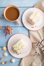 Roll biscuit cake with cream cheese and jam, cup of coffee on blue wooden background and linen