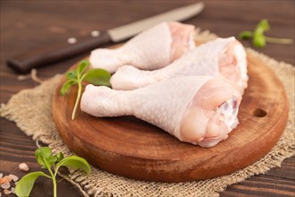 Raw chicken legs with herbs and spices on a wooden cutting board on a brown wooden background and