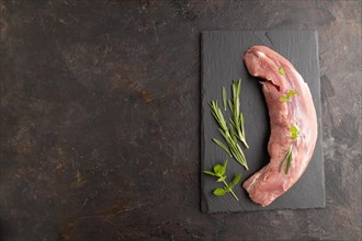 Raw pork meat with herbs and spices on slate cutting board on black concrete background. Top view,