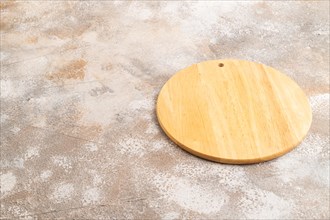 Empty round wooden cutting board on brown concrete background. Side view, copy space