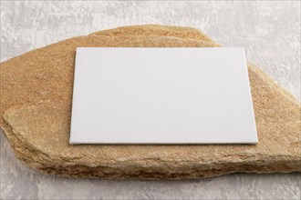 White paper business card, mockup with natural stone on gray concrete background. Blank, side view,