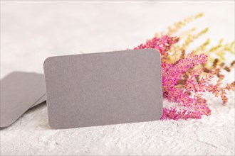 Gray paper business card mockup with purple astilbe flowers on gray concrete background. Blank,