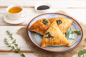 Homemade asian pastry samosa, cup of green tea on white wooden background and linen textile. side