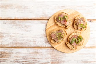 Bread sandwiches with jerky salted meat, sorrel and cilantro microgreen on white wooden background.
