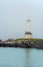 White lighthouse with turtle roof on rocky outcropping in Jeju, South Korea, Asia