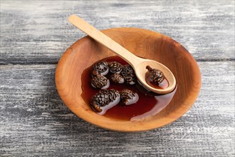 Pine cone jam in wooden bowl on gray wooden background. Side view, close up