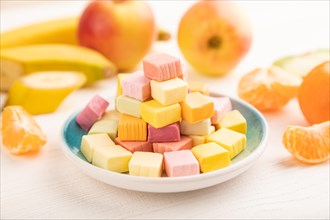 Various fruit jelly chewing candies on plate on white wooden background. apple, banana, tangerine,