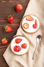 Grained cottage cheese with strawberry jam on brown wooden background and linen textile. top view,