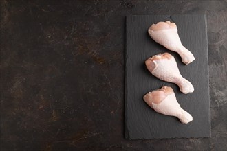 Raw chicken legs on a black slate cutting board on a black concrete background. Top view, flat lay,