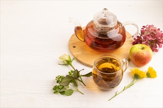 Red tea with herbs in glass teapot on white wooden background. Healthy drink concept. Top view,