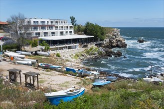 A hotel on the rocky coast with a view of the sea and several boats moored on the beach, harbour