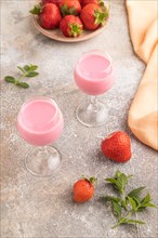 Sweet strawberry liqueur in glass on a gray concrete background and orange textile. side view,